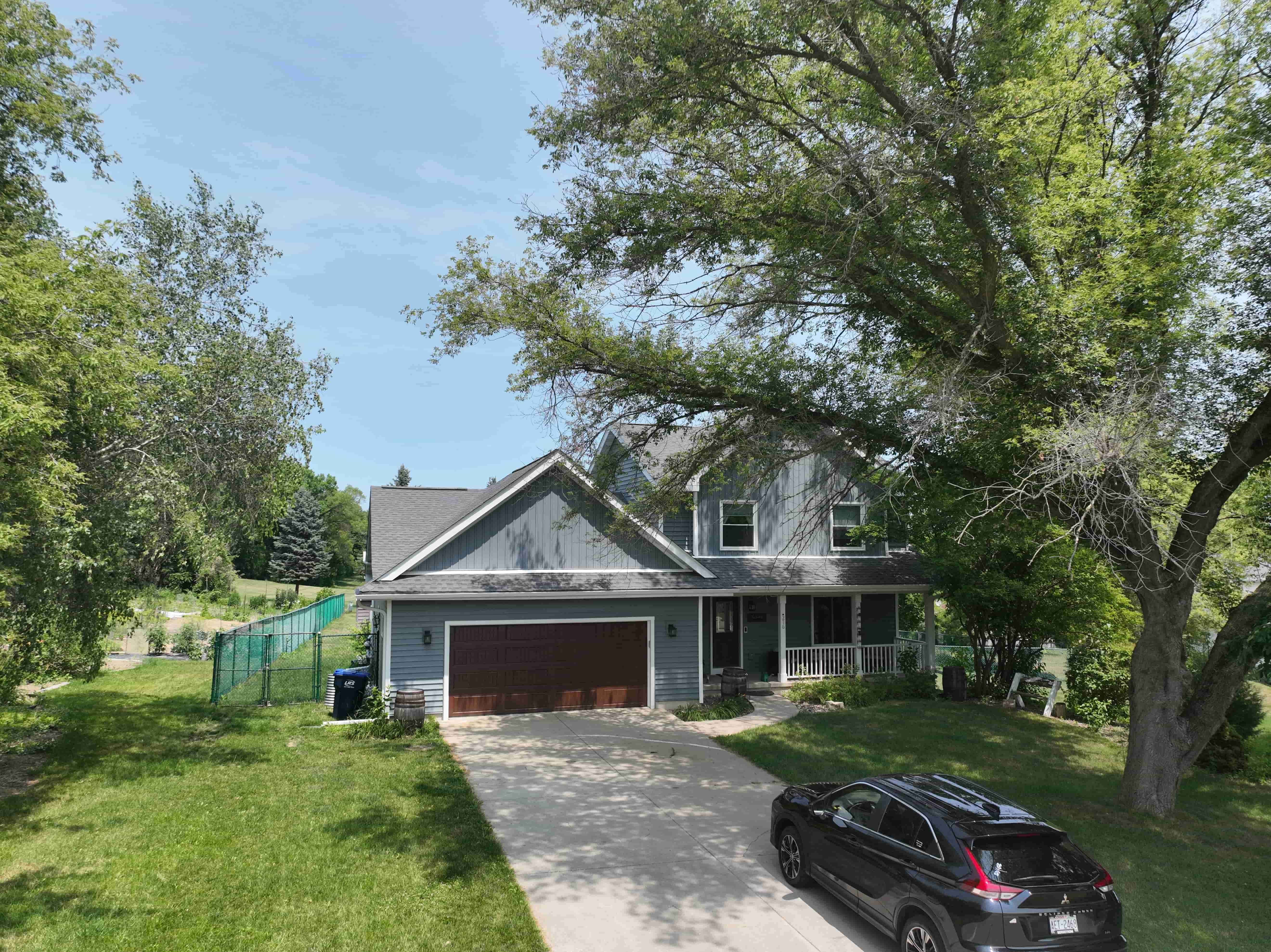 Updated home exterior with new gray siding and roof, front porch, and large tree in suburban Madison neighborhood