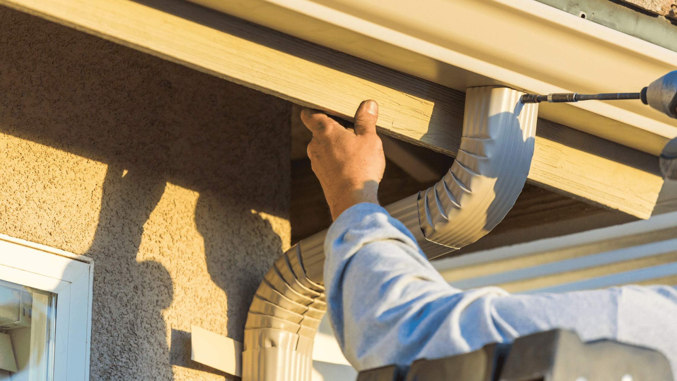 A contractor installs a seamless aluminum gutter and downspout along a home's roofline, ensuring proper drainage and long-term protection for the exterior.